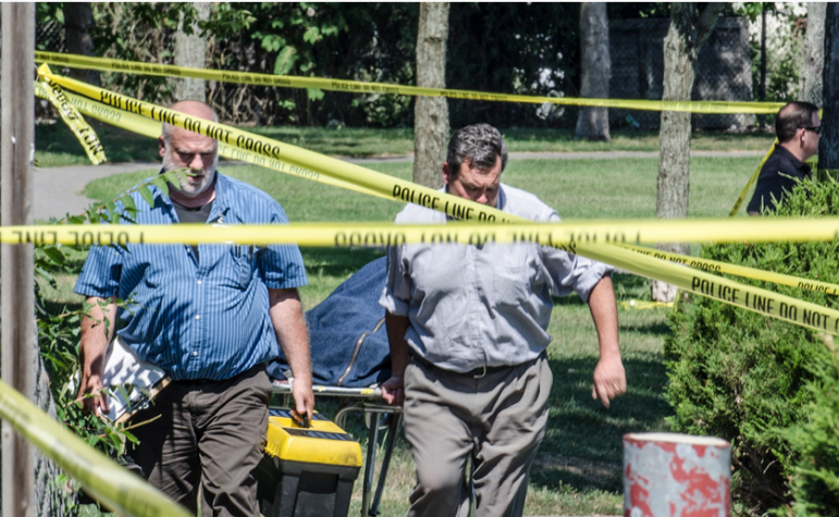 A member of the NH State Medical Examiners office escorts the body of the homicide victim from the scene at Prout's Park in Manchester. The victims body was being brought to Concord to the Coroners office for a autopsy.