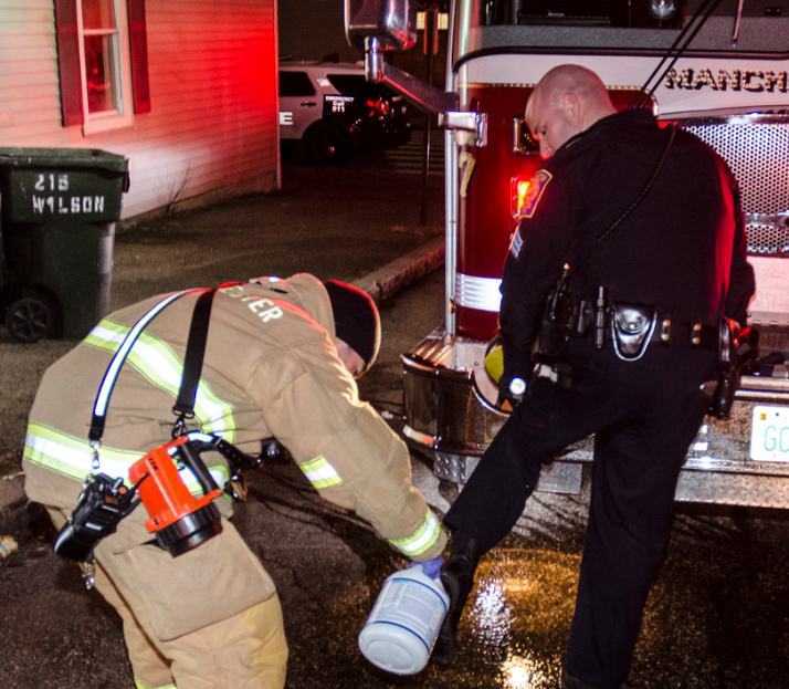 A Manchester firefighters assists a Manchester Police officer by helping to sanitize his shoes after entering an apartment with animal feces throughout.